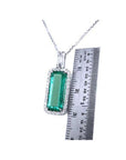 Elongated natural emerald pendant with halo diamonds in 18K white gold, shown next to a ruler.