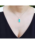 Elongated natural emerald pendant with halo diamonds on an 18K white gold chain, worn on a woman's neck.