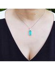 Elongated natural emerald pendant with halo diamonds on an 18K white gold chain, worn on a woman's neck.