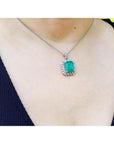7.78 ct. natural emerald pendant with halo diamonds in 14K white gold, worn on a necklace.