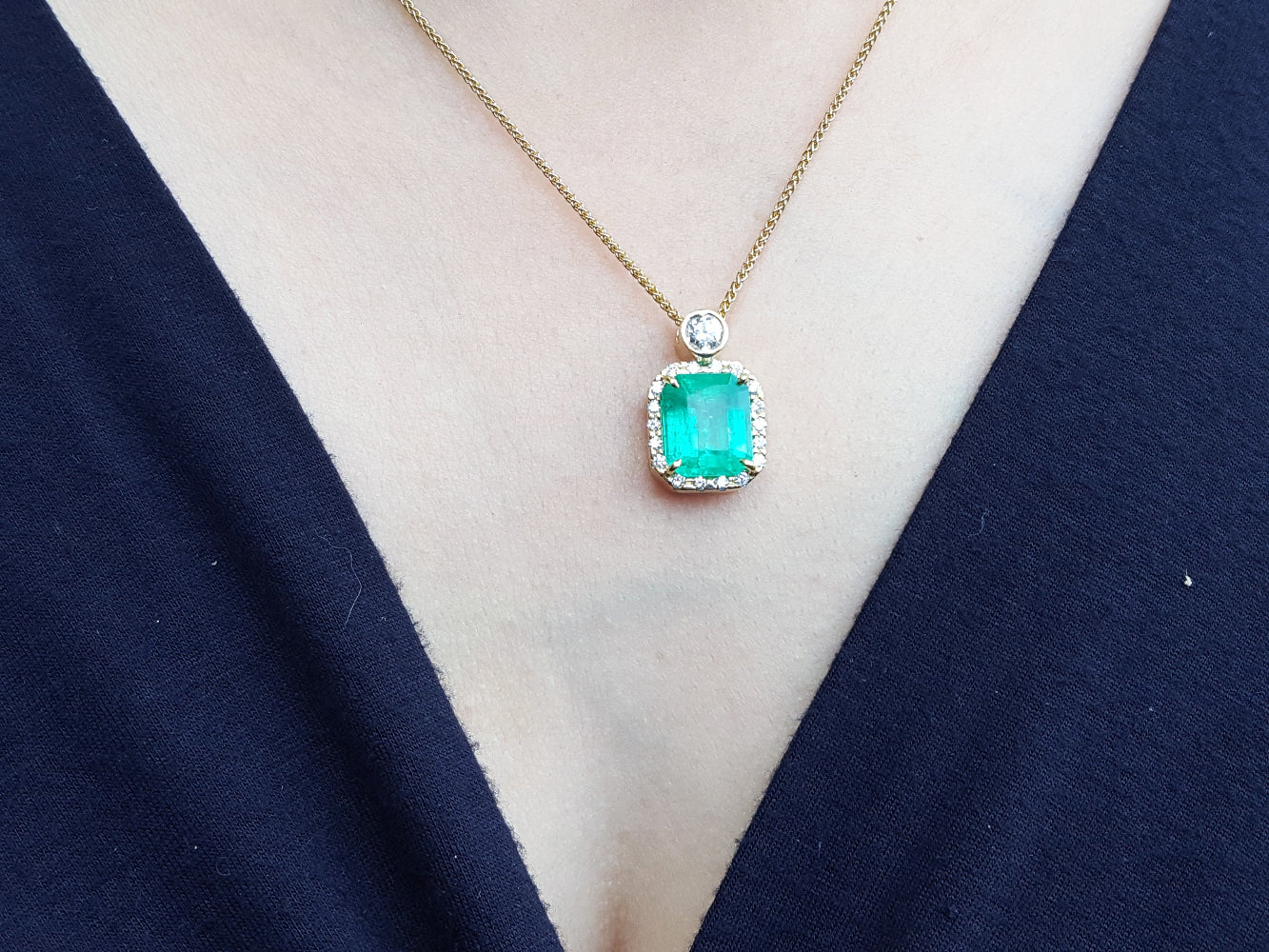 Gold necklace with a natural emerald pendant on a woman's neck.