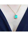 7.09 ct. natural emerald pendant necklace with halo diamonds on an 18K yellow gold chain.