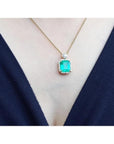 7.09 ct. natural emerald pendant necklace with halo diamonds on an 18K yellow gold chain.