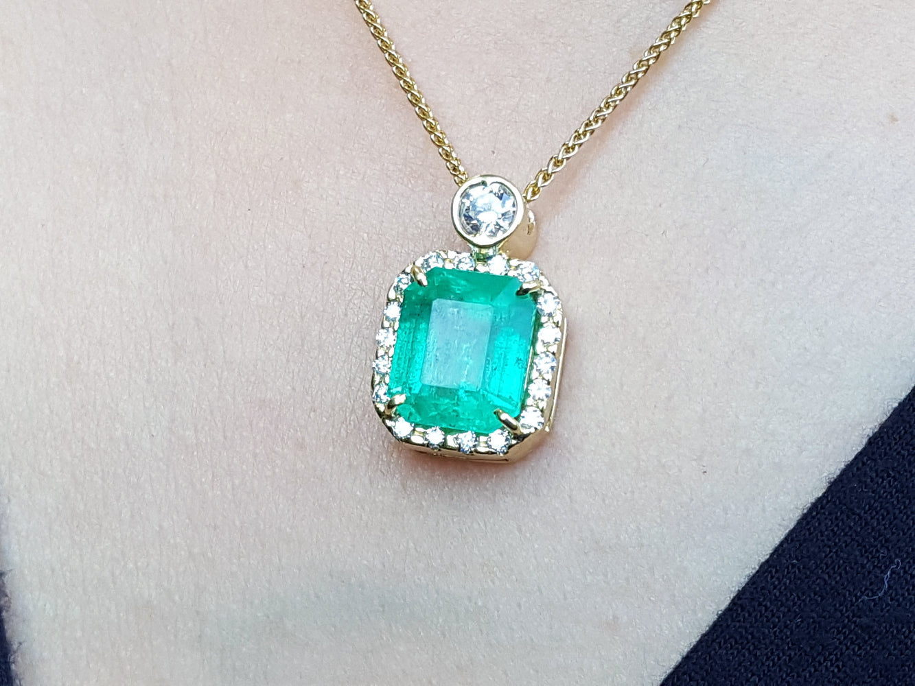 Gold necklace with a square emerald pendant on a skin background.