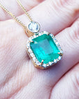 Emerald rectangular shaped pendant on a gold chain held on a hand.