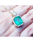 Emerald rectangular shaped pendant on a gold chain held on a hand.
