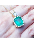 7.09 ct. natural emerald pendant necklace with halo diamonds on an 18K yellow gold chain.