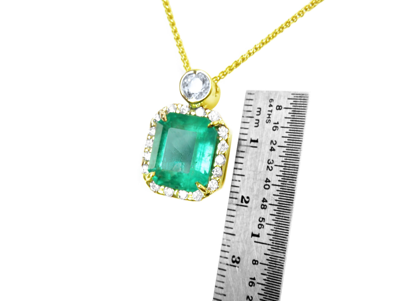 Gold necklace with an emerald pendant next to a ruler for scale on a white background