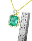 Gold necklace with an emerald pendant next to a ruler for scale on a white background