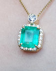 A square natural colombian emerald in a halo diamond pendant made in 18k yellow gold topside view.