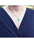 Emerald pendant necklace with diamond halo on an 18K yellow gold chain, worn on a woman's chest.