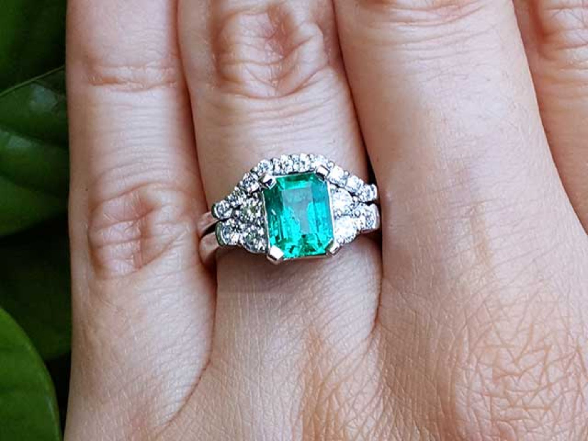 A real Colombian emerald and matching band ring on a finger against a natural background.