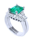 A partial lateral profile view of the emerald on top with side diamonds ring with matching band together.
