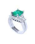 A partial lateral profile view of the emerald on top with side diamonds ring with matching band together.