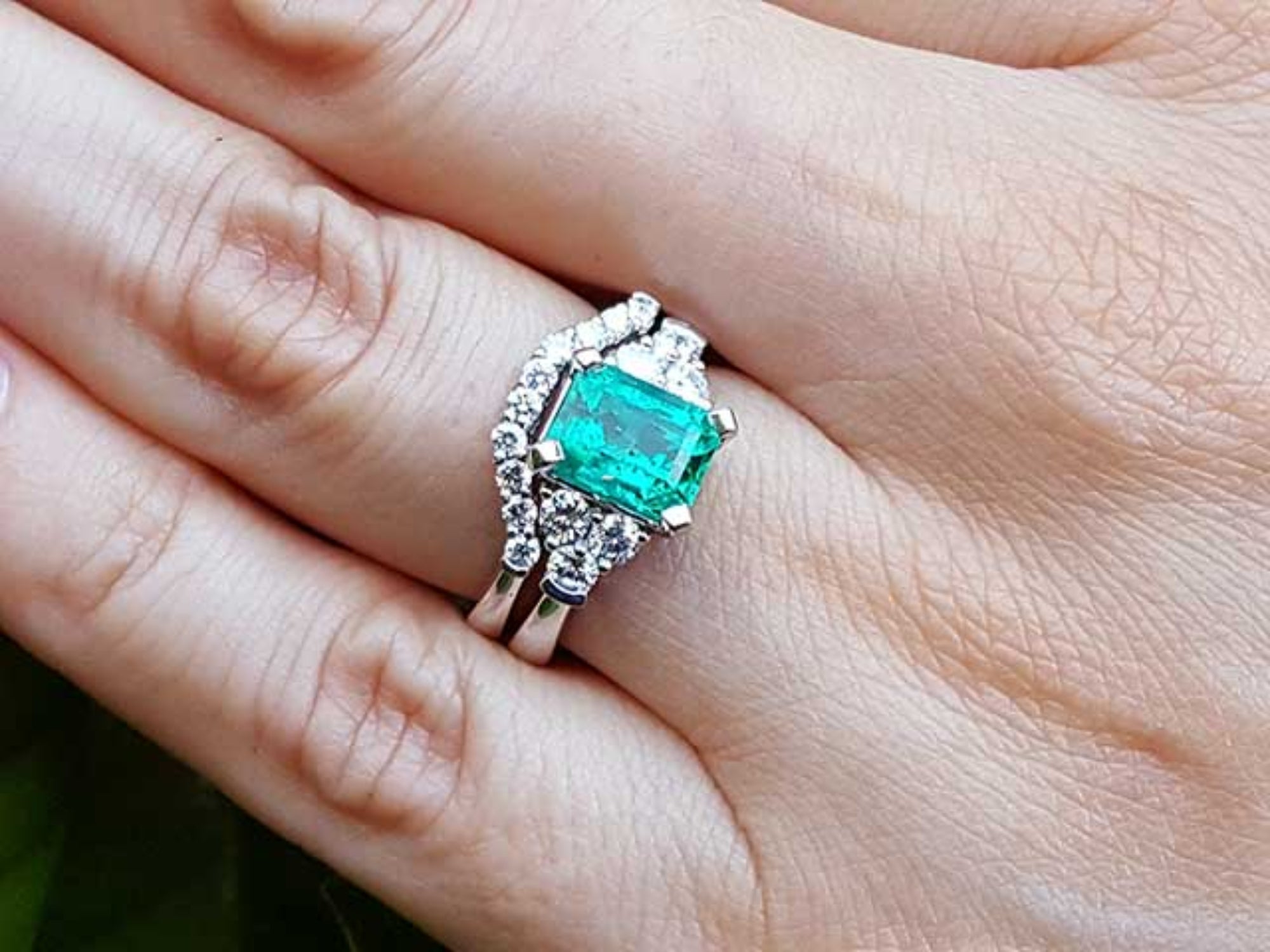 A Muzo born emerald on top of the ring with the matching wedding band on a person's finger.