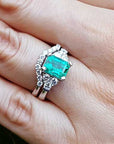 A Muzo born emerald on top of the ring with the matching wedding band on a person's finger.