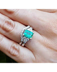A Muzo born emerald on top of the ring with the matching wedding band on a person's finger.