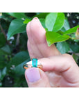 Hand holding a Colombian emerald ring with a green gemstone against a leafy background.