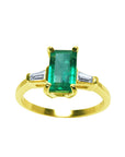 A 14k yellow gold ring with an emerald and two side baguette diamonds on a white background.