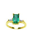 A 14k yellow gold ring with an emerald and two side baguette diamonds on a white background.