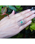 Hand wearing a silver ring with a real colombian emerald against a green leafy background.