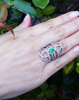Hand wearing a silver ring with a real colombian emerald against a green leafy background.