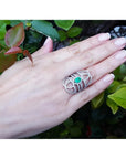 Sterling silver ring with oval natural emerald, CZ halo, and intricate filigree design on a hand.