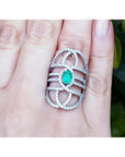 Sterling silver ring with oval natural emerald and CZ halo accent on a woman's finger.