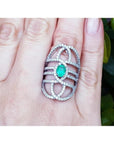 Sterling silver ring with oval natural emerald and CZ halo accent on a woman's finger.