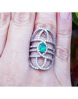 Silver ring with a natural oval emerald on a person's finger.