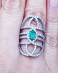 Silver ring with a natural oval emerald on a person's finger.