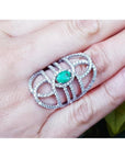 Sterling silver ring with a natural oval emerald center and CZ halo, featuring an intricate filigree design.