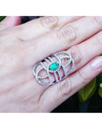 Silver ring with a Muzo colombian emerald on a hand against a natural background.