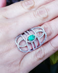 Silver ring with a Muzo colombian emerald on a hand against a natural background.