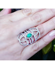 Sterling silver ring with oval emerald center and CZ halo on a woman's hand.