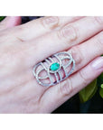 Sterling silver ring with oval emerald center and CZ halo on a woman's hand.