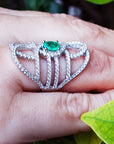 Silver ring with a oval cut natural emerald on a hand with a leaf background.