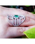 Sterling silver ring with oval natural emerald and CZ halo accent on a hand.
