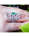 Sterling silver ring with oval natural emerald and CZ halo accent on a hand.
