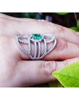 Sterling silver ring with oval natural emerald and CZ halo accent on a hand.