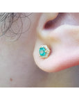 An earlobe waring an emerald and halo diamond stud earring in 14k yellow gold.