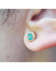 An earlobe waring an emerald and halo diamond stud earring in 14k yellow gold.