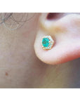 Hexagon emerald and diamond stud earring in 14K yellow gold, worn on an ear.
