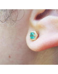 Hexagon emerald and diamond stud earring in 14K yellow gold on an ear.
