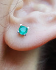 Close-up of an ear with a round cut emerald stud earring.