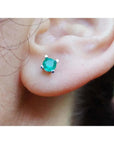 Close-up of an ear with a round cut emerald stud earring four prong setting in 1k yellow gold.