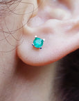 Close-up of an ear wearing a emerald gemstone earring with a blurred natural background.