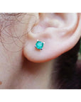 Close-up of an ear wearing a emerald gemstone earring with a blurred natural background.