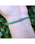 A white gold emerald tennis bracelet on a wrist with a natural background.
