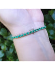 Colombian emerald tennis bracelet with round green emeralds in 14K white gold on a wrist.